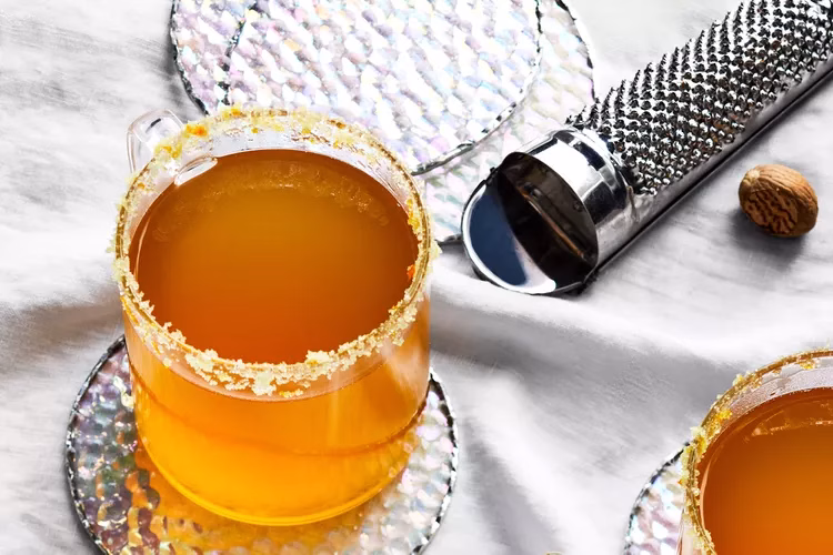 An orange cocktail in a stemless wine glass with a grater and sugar zest rim