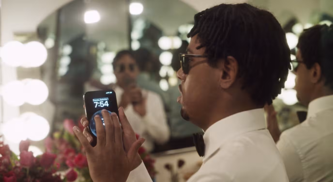 A blind person wears dark sunglasses and uses an Apple phone to identify objects in a room