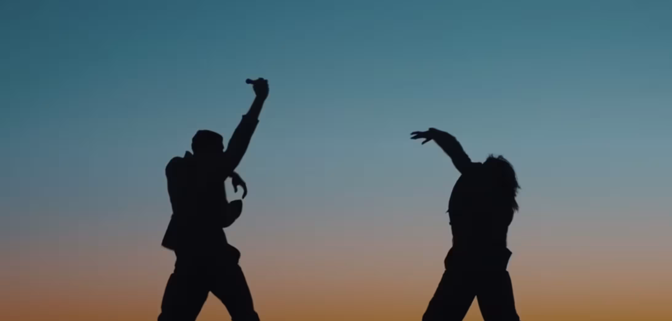 Two human figures dance before a dusk sky