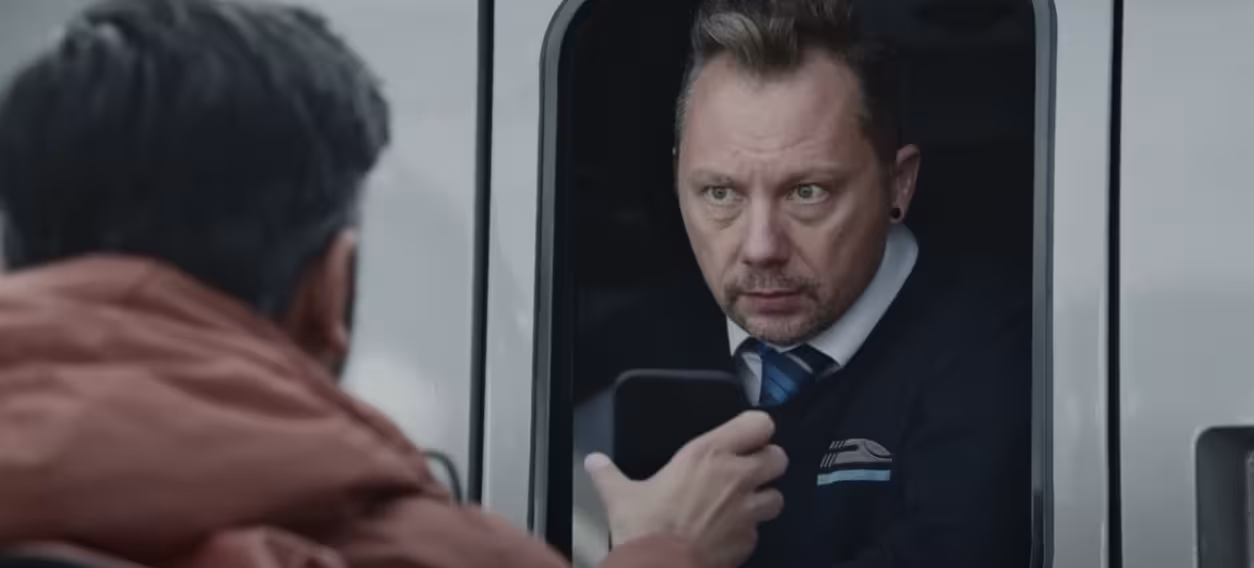 A man shows his phone screen to a conductor seated in a train