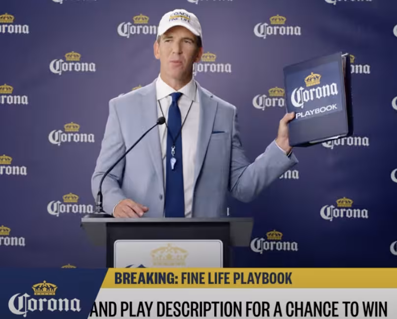 Eli Manning holds up a Corona Extra playbook behind a podium